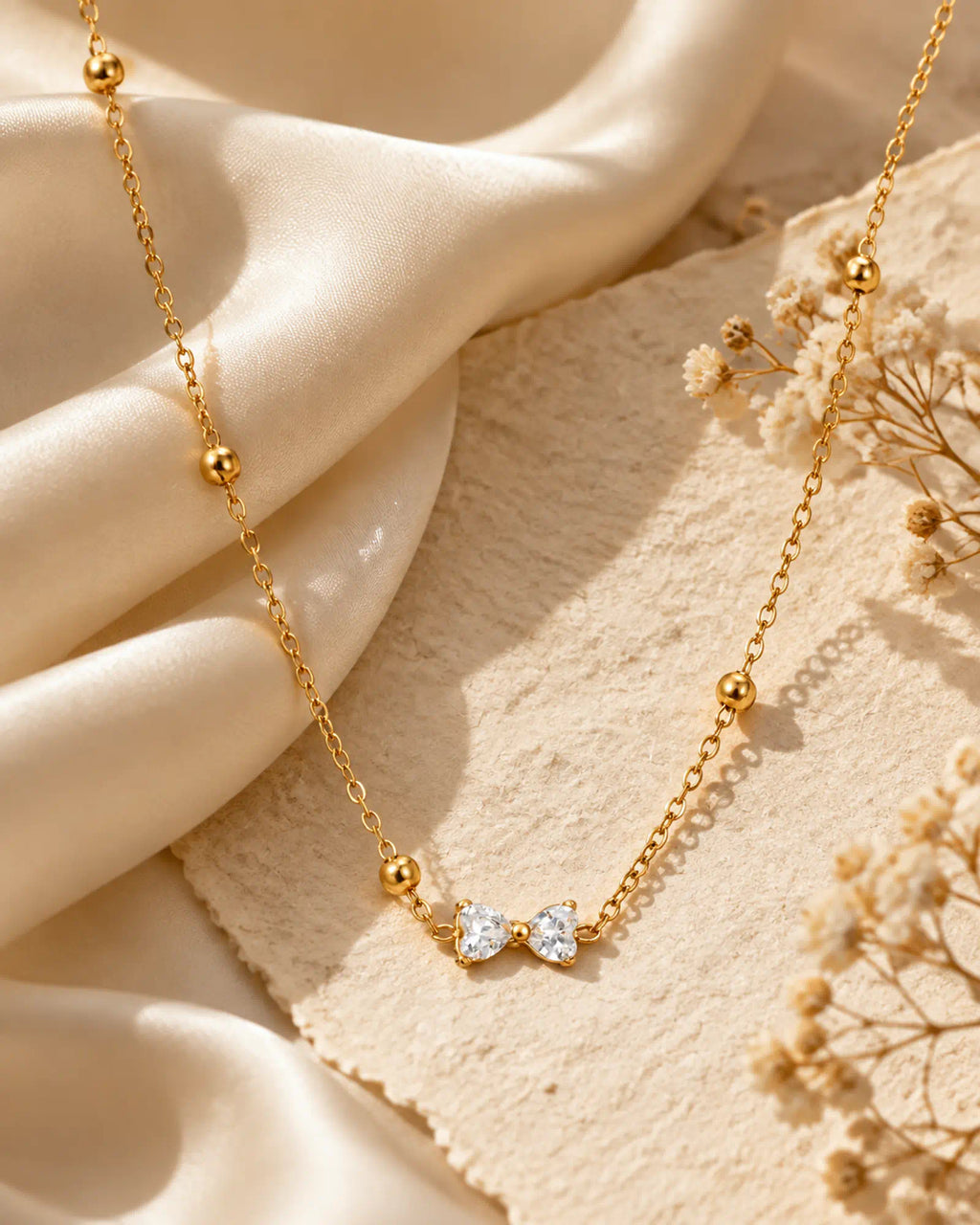 Wearlumi Beaded Bow Pendant Necklace draped over champagne silk fabric