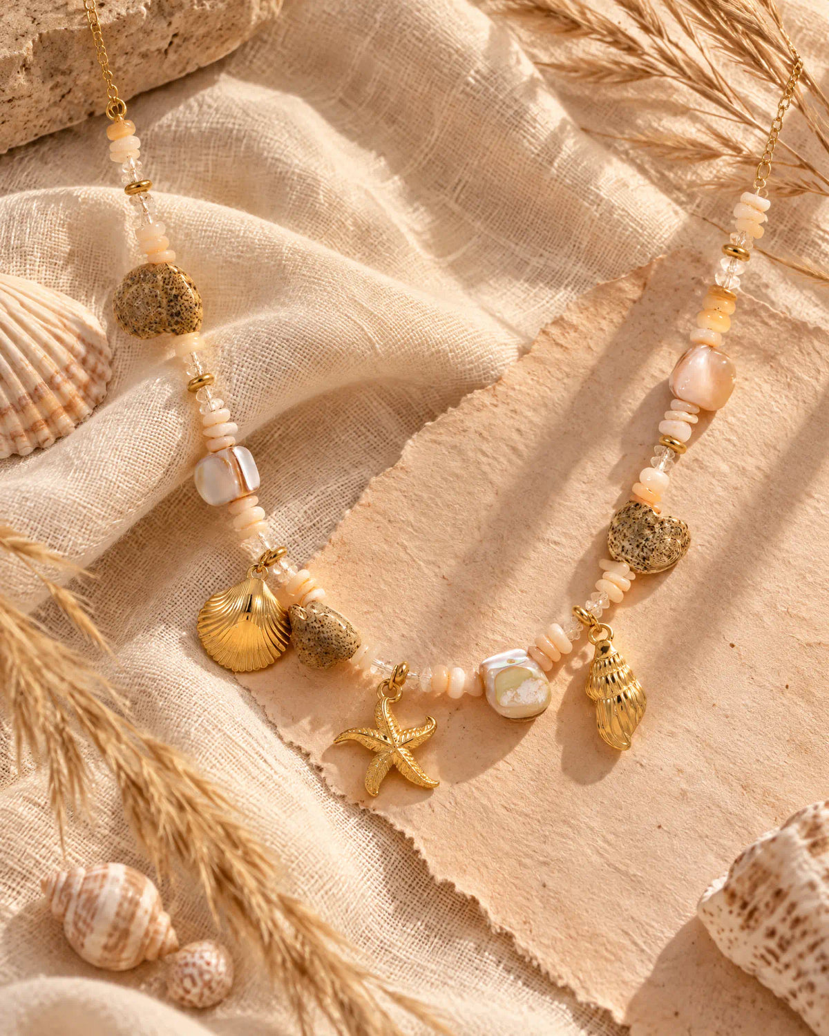 Shoreline Starfish Charm Necklace arranged on textured linen fabric with seashells