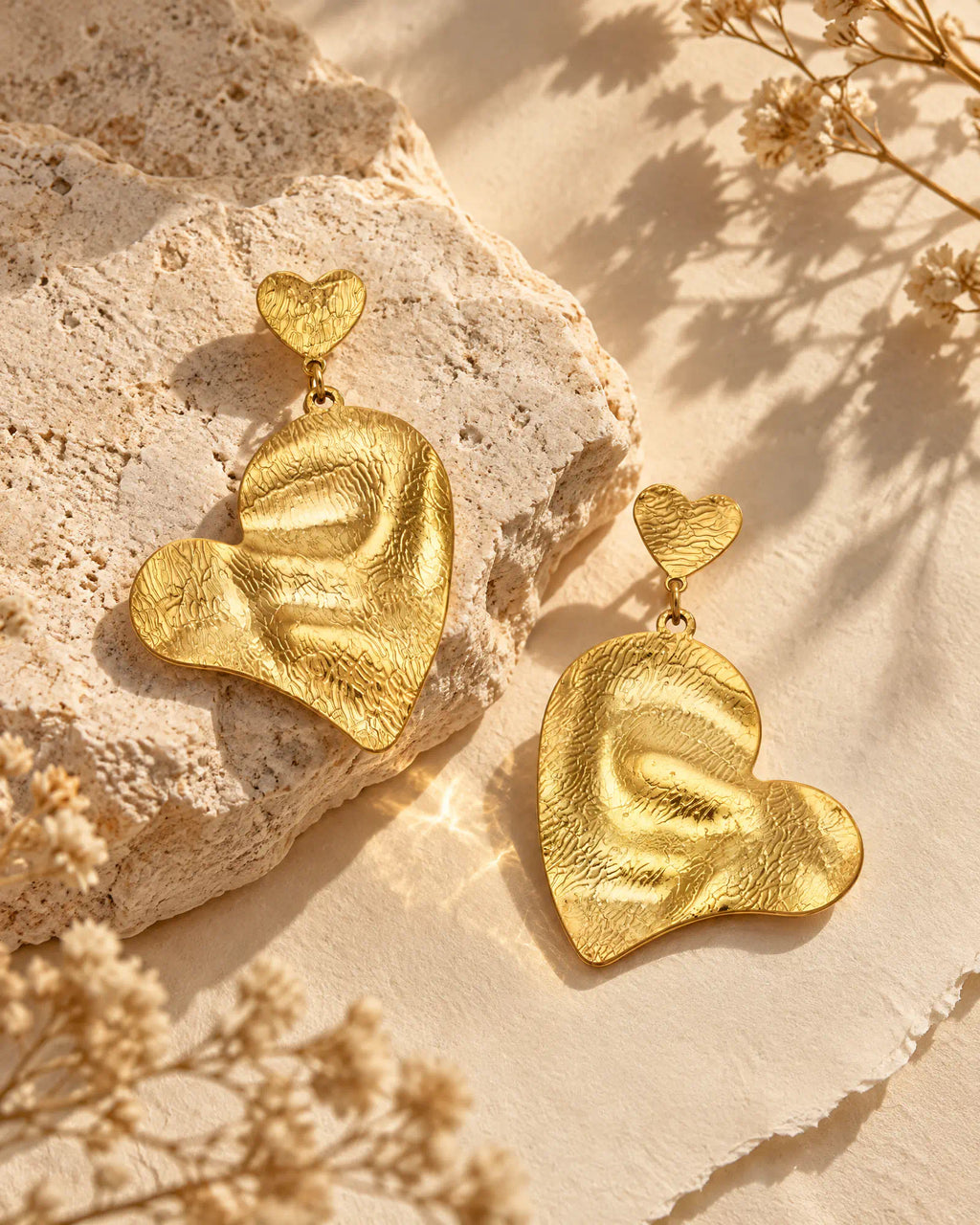 Rippled heart drop earrings resting on neutral limestone