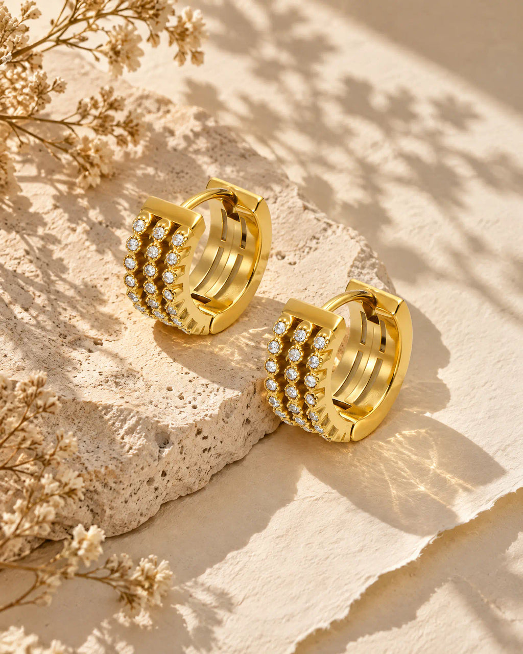 Triple row huggie hoop earrings resting on textured limestone
