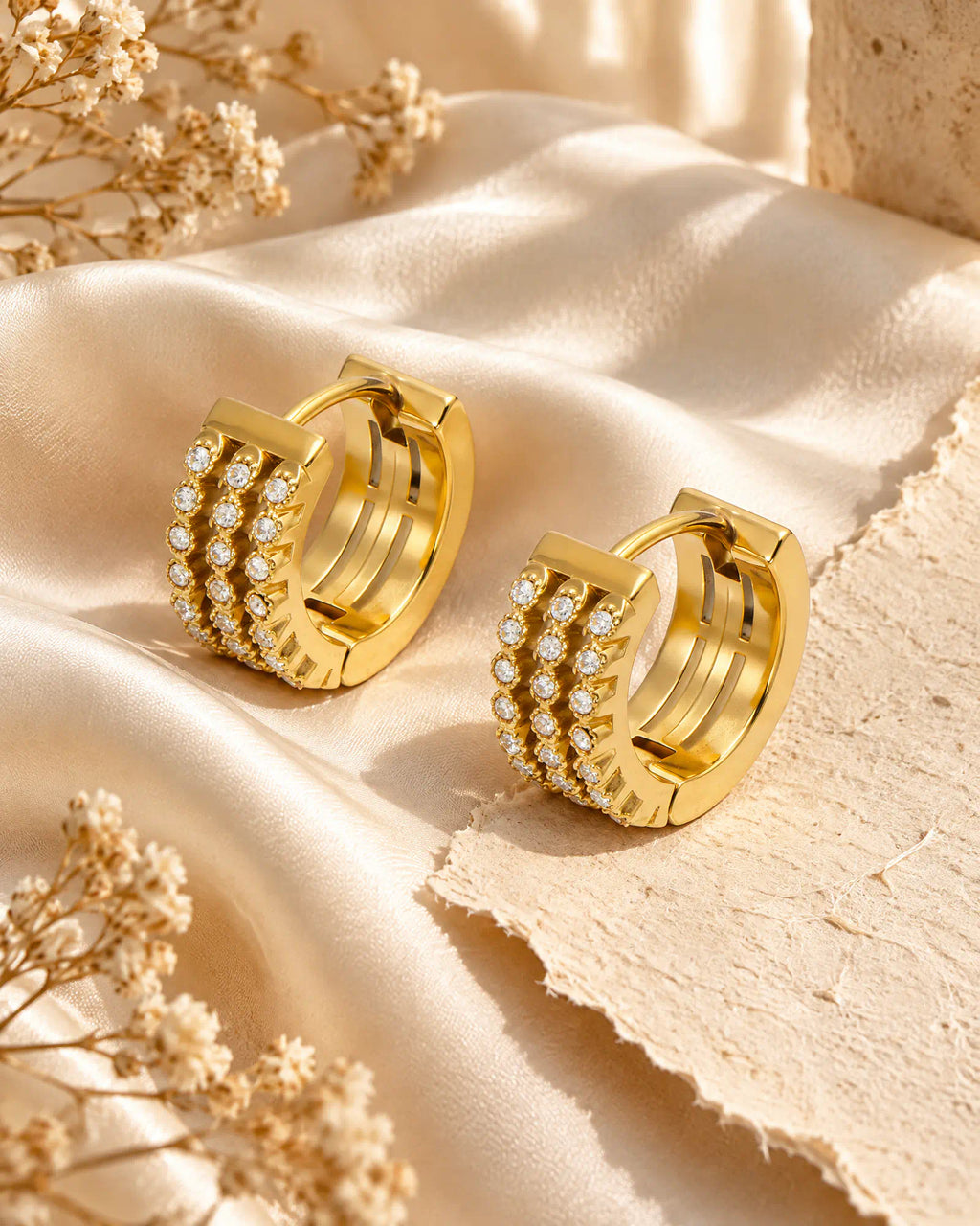 Triple row huggie hoop earrings displayed on silk cloth